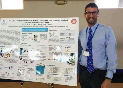 Student presenter standing next to their poster at the KU/Haskell Undergraduate Research Symposium